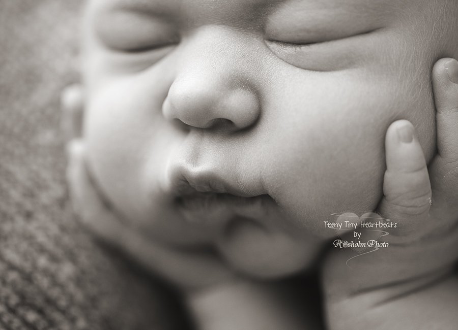 Close up billede af nyfødt ansigt i sort hvid med hænderne på kinderne