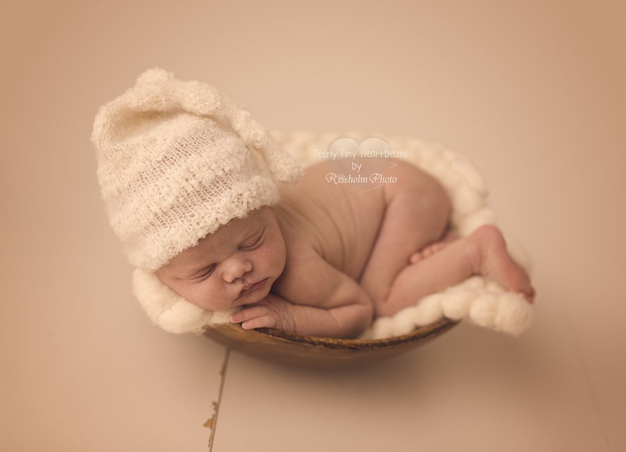 billede af sovende nyfødt i træskål med hvid hue