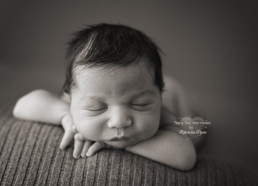 sort hvid billede af nyfødt sovende på maven med hænderne under hovedet