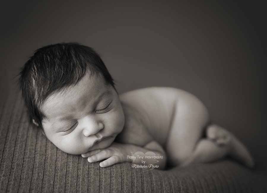 sort hvid billede af nyfødt sovende på maven på tæppe