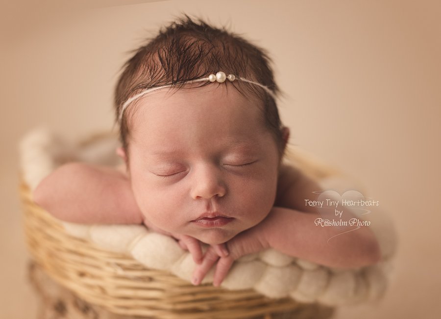 spædbarn fotograferet med hænderne under hagen i kurv med perle pandebånd.