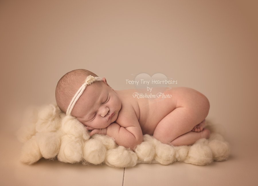 sovende nyfødt pige med pandebånd på maven på cremet tæppe hos fotograf