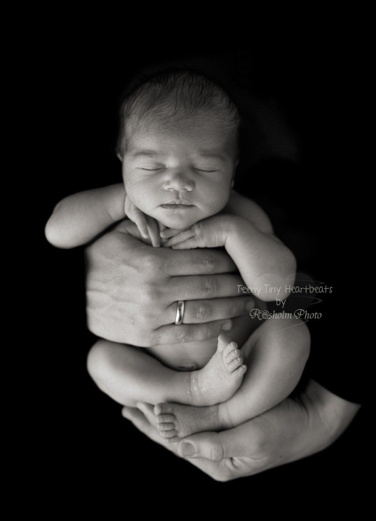 nyfødt fotograferet i fars hænder sovende i sort hvid